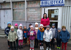 Dzieci stoją przed Biblioteką Miejską wraz z panią bibliotekarką