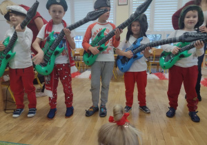 Piątka chłopców ubrana w biało-czerwone stroje i czapki żołnierskie gra na dmuchanych gitarach