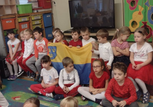 Dzieci z grupy V trzymają flagę Pabianic podczas śpiewania piosenki o symbolach narodowych