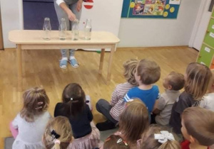 Dzieci obserwują jak pani gra na butelkach z różńną ilością wody