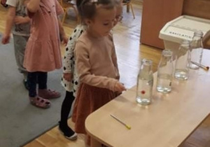 Dziewczynka gra na butelkach z wodą, pozostałe dzieci czekają w kolejce