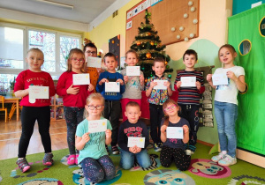 Dzieci z grupy IV stoją przed ubraną choinką i pokazują swoje listy do świętego Mikołaja