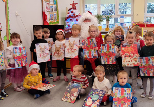 Dzieci z grupy II stoją przed Mikołajem i pokazują swoje kalendarze adwentowe, które dostały od Mikołaja