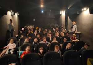 Przedszkolaki siedzą w fotelach w kinie i czekają na wyświetlanie bajki