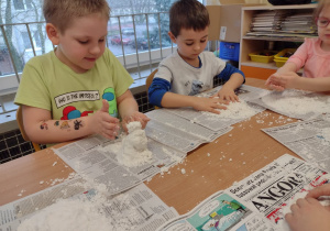 Troje dzieci z grupy V próbuje ulepić ze sztucznego śniegu bałwanki