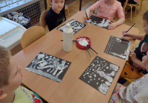 Starszaki z grupy V malują zimowy obrazek białą farbą na czarnym kartonie