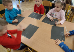 Dzieci z grupy V rysują zimowe pejzaże białą kredką na czarnym tle