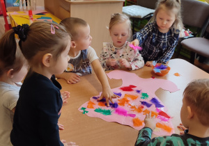 Sześcioro dzieci wykleja sukienkę z papieru kolorowymi piórkami