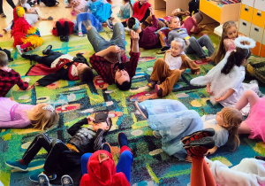 Przedszkolaki leżą podczas zabawy na dywanie z wodzirejem