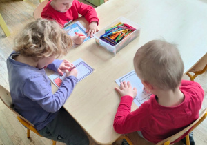Troje przedszkolaków z grupy II koloruje papierowe tablety