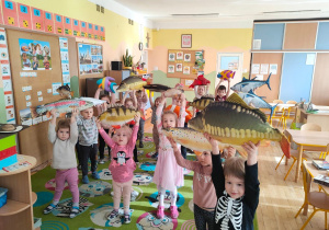 Dzieci z grupy pierwszej i drugiej trzymają w rękach duże modele ryb