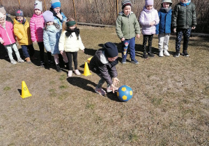 Dzieci z grupy trzeciej po kolei będą turlać piłkę pod górę
