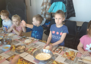 Pięcioro dzieci stoi przy stolikach, na których są gotowe kulki ciasta na pizze