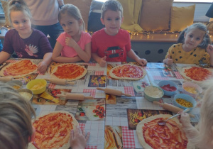 Czworo dzieci ma posmarowaną pizzę pomidorowym sosem