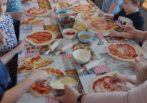 Przedszkolaki nakładają ser starty na swoje pizze