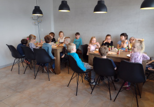 Dzieci siedzą przy stolikach i jedzą wykonane przez siebie pizze