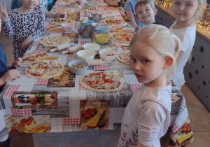 Przedszkolaki stoją przy swoich pizzach i czekają aż polacki trafią do pieca