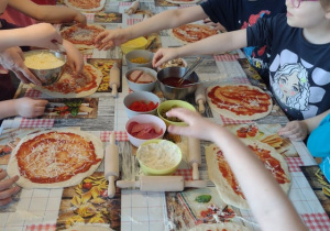 Dzieci posypują swoje pizze startym serem