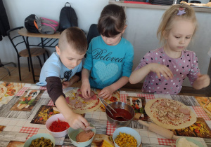 Troje dzieci nakłada składniki na swoje pizze