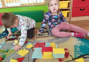 Dwoje dzieci układa obrazki z klocków w kształcie figur