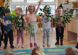 Pięcioro dzieci z najmłodzsej grupy macha zielonymi gałązkami
