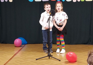 Chłopiec i dziewczynka stoją przy mikrofonie i śpiewają piosenkę