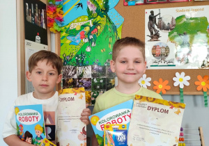Dwóch chłopców pokazuje swoje dyplomy i nagrody - kredki i kolorowanki