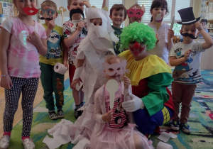Dzieci z klaunem stoją przy dziewczynce owiniętej w papier toaletowy - mumię