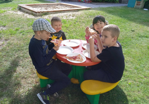 Czworo dzieci siedzi przy stoliczku i je pizzę