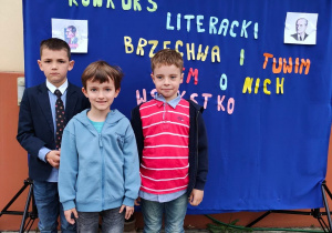Trzech chłiopców stoi przed dekoracją z tkaniny z napisem Brzechwa i Tuwim, wiem o nich wszystko