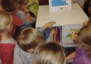 Dzieci ze starszych grup oglądają książki stojące na regale Zaczytanej Biblioteki