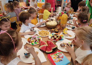 Dzieci z grupy III siedzą przy stolikach i zajadają słodkości przygotowane przez rodziców