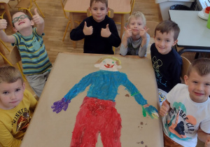 Chłopcy z grupy piątej siedzą wokół namalowanego przez siebie przedszkolaka