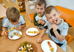 Trzech chłopców je przygotowane przez siebie owocowe szaszłyki