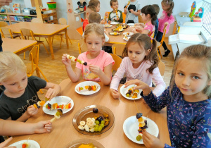 Cztery dziewczynki jedzą przygotowane przez siebie owocowe szaszłyki