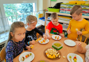 Czworo dzieci przygotowuje owocowe szaszłyki