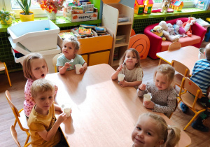 Sześcioro dzieci siedzi przy stoliku i je mus owocowy