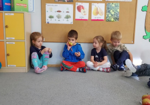 Dzieci siedza w kole i oglądają i wąchają owoce