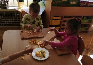 Dwoje dzieci kroi owocę na sałtkę