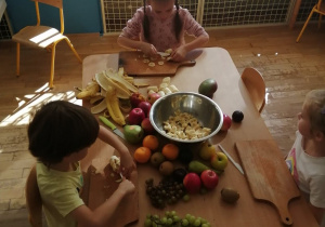 Troje dzieci kroi owoce na mniejsze kawałki