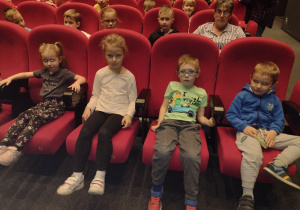 Ośmioro dzieci siedzi w fotelach przed przedstawieniem