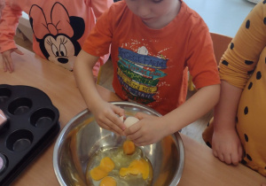 Chłopiec wbija jajko do miski