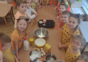 Dzieci z grupy V stoją przy stole ze składnikami na babeczki