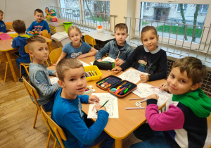 Dzieci z grupy piątej siedzą przystoliku i kolorują obrazki przedstawiające dzieci z różnych stron świata
