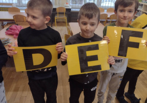 Trzech chłopców trzyma litery z alfabetu do piosenki