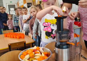 Dzieci z grupy piątej wkładają marchewki i jabłka do sokownika