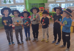 Siedmioro chłopców w czapkach góralskich grają na grzechotkach podczas śpiewania kolędy