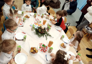 Dzieci siedzą przy stole, na którym jest poczęstunek przygotowany przez rodziców