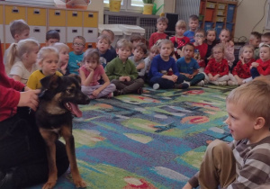Pies Hera przypatruje się dzieciom siedzącym na dywanie