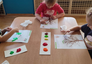 Dzieci malują palcami jesienne drzewka